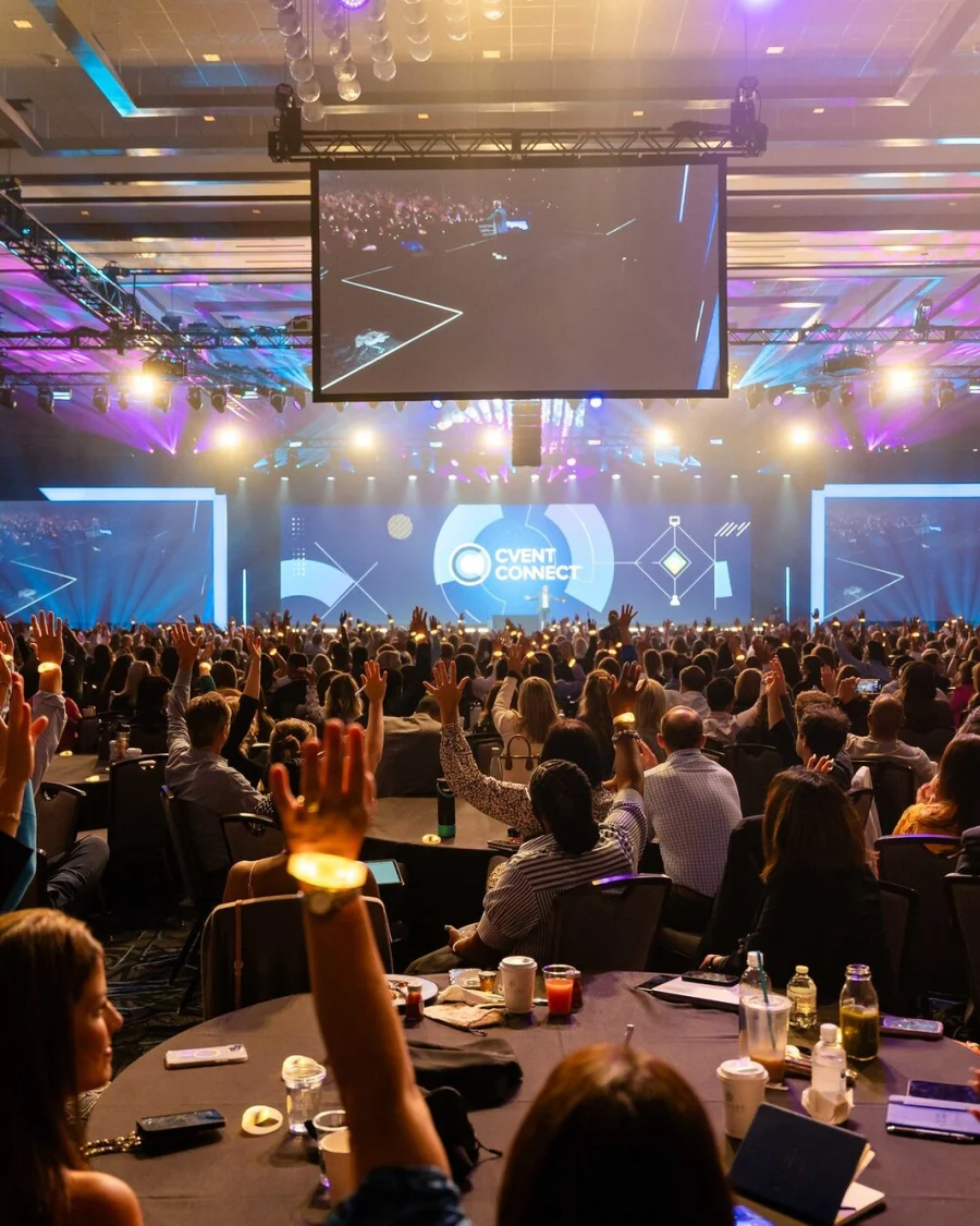 A large conference hall with an audience facing a lit stage