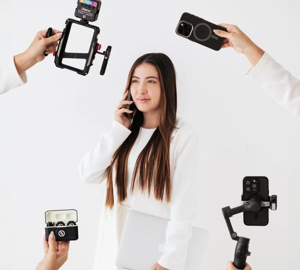 A creator holding camera gear and a phone on a white background