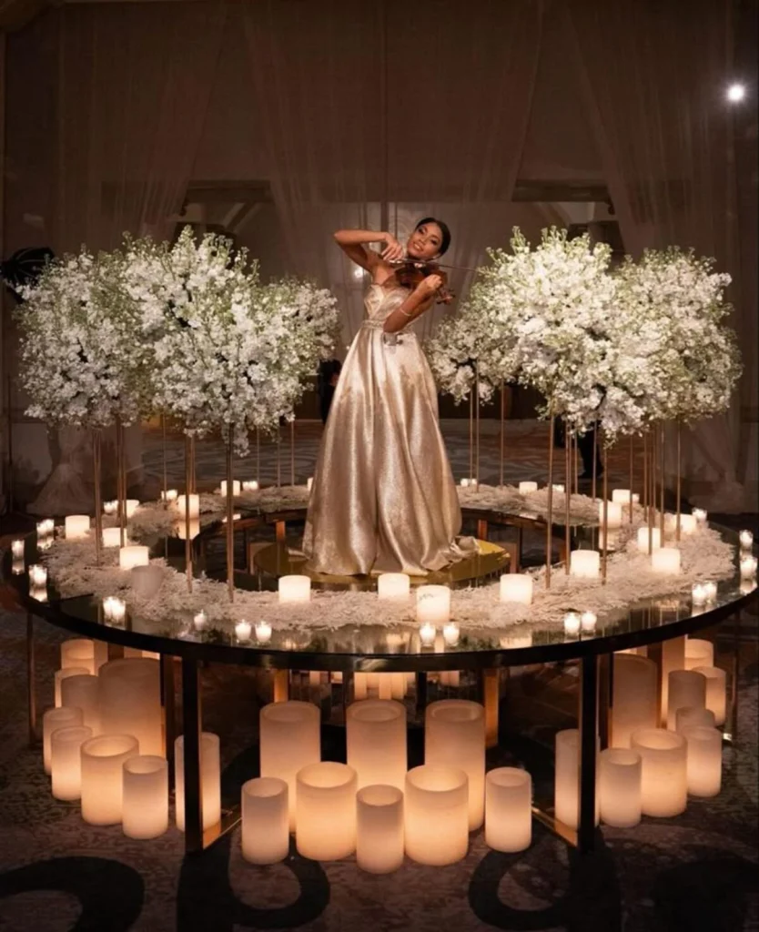 A bride surrounded by candles and white blossom on a circular stage