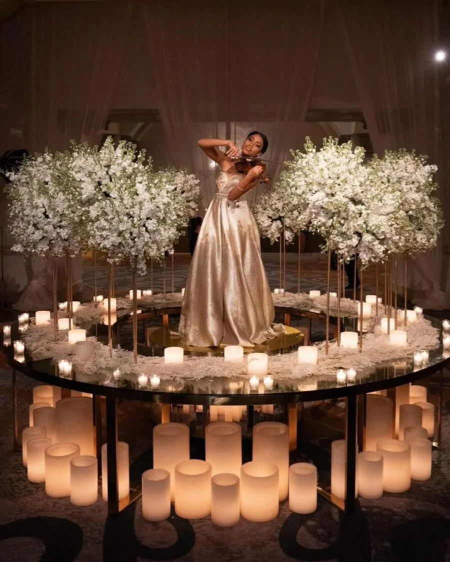 A bride surrounded by candles and white blossom on a circular stage